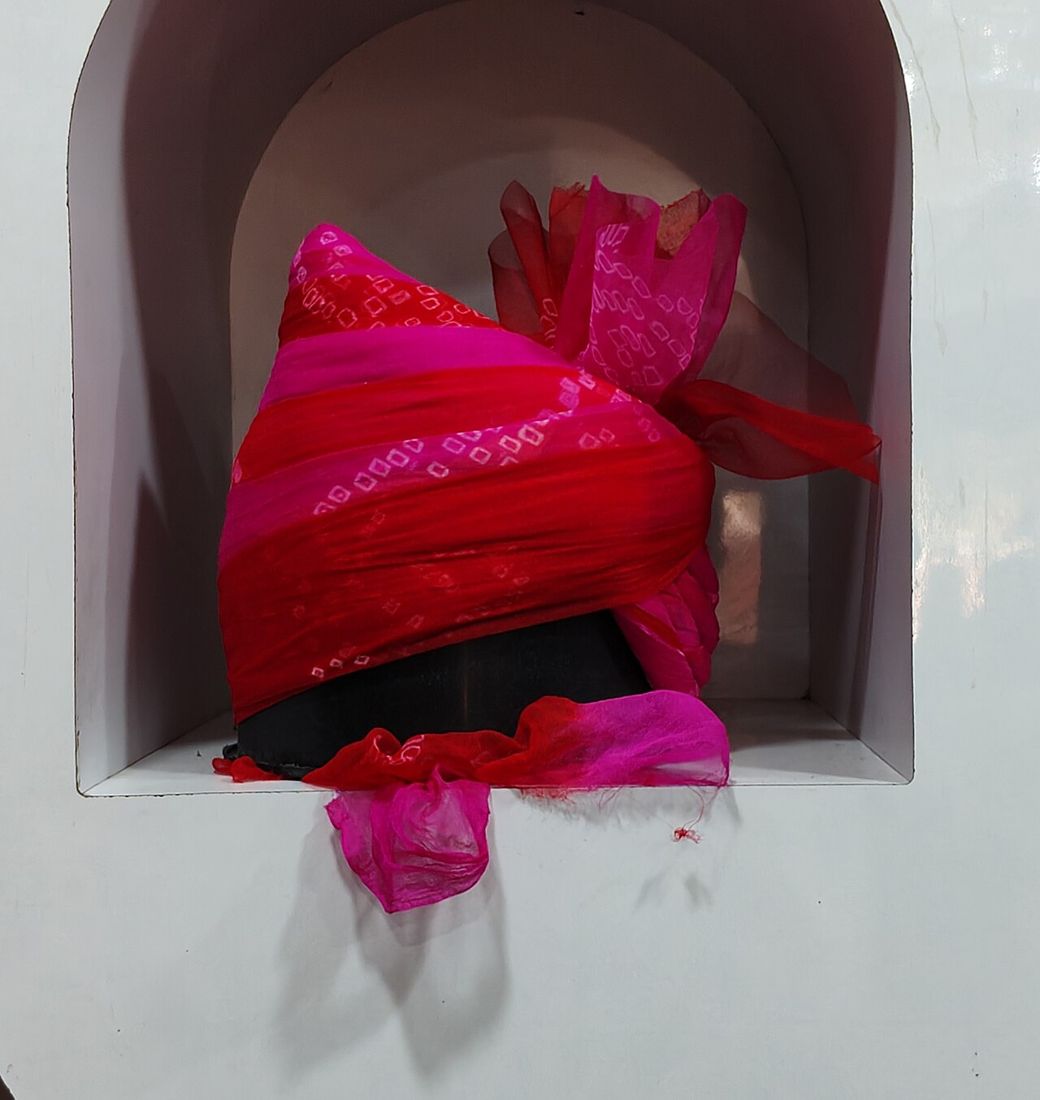 Red and pink bandhani safa with a loose tail, on a display stand